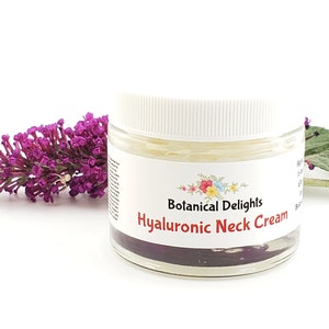 Op de afbeelding: Een witte pot met een wit deksel, gevuld met een gele cr&egrave;me. De pot heeft een etiket met de tekst "Botanical Delights Hyaluronic Neck Cream".