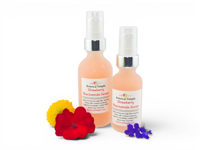 May include: Two bottles of Botanical Delights Strawberry Niacinamide Serum with white pump tops. The bottles are filled with a pink liquid and have labels. A yellow flower, a red flower, and a cluster of blue flowers are in front of the bottles.