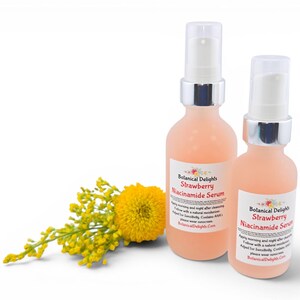 May include: Two peach-colored serum bottles with silver pumps and white labels that read "Botanical Delights Strawberry Niacinamide Serum." A yellow flower and sprig of yellow flowers are in the lower left corner. The bottles are on a white background.