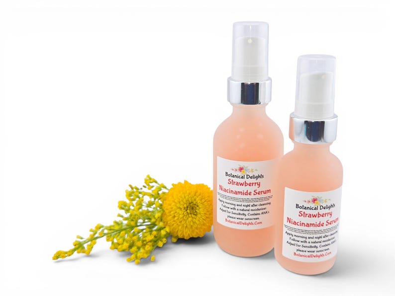 May include: Two peach-colored serum bottles with silver pumps and white labels that read "Botanical Delights Strawberry Niacinamide Serum." A yellow flower and sprig of yellow flowers are in the lower left corner. The bottles are on a white background.