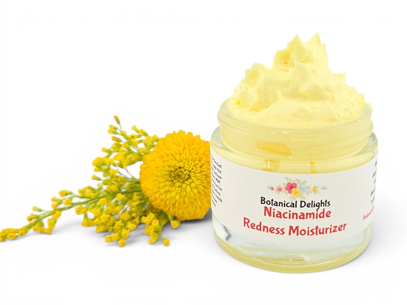May include: A jar of yellow moisturizer with the text "Botanical Delights Niacinamide Redness Moisturizer" on the label. A yellow flower and sprig of yellow flowers are to the left of the jar. The background is white.