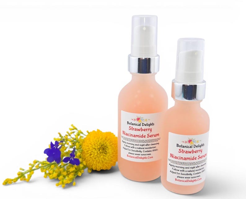 May include: Two peach-colored serum bottles with silver accents and white pumps. The bottles have labels that read "Botanical Delights Strawberry Niacinamide Serum." A small bouquet of yellow and blue flowers sits to the left of the bottles.