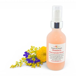 May include: A peach-colored serum bottle with a white pump and silver collar. The label reads "Botanical Delights Strawberry Niacinamide Serum." A small bouquet of yellow and purple flowers is to the left of the bottle. The background is white.