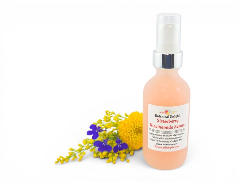 May include: A peach-colored serum bottle with a white pump and silver collar. The label reads "Botanical Delights Strawberry Niacinamide Serum." A small bouquet of yellow and purple flowers is to the left of the bottle. The background is white.