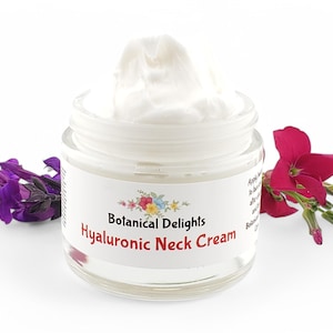Op de afbeelding: Een witte pot Hyaluronzuur Halscr&egrave;me van Botanical Delights. De pot is open en de cr&egrave;me is zichtbaar. De pot is omringd door paarse en roze bloemen.