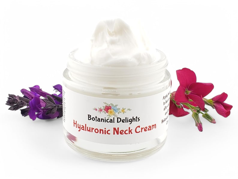 Op de afbeelding: Een witte pot Hyaluronzuur Halscr&egrave;me van Botanical Delights. De pot is open en de cr&egrave;me is zichtbaar. De pot is omringd door paarse en roze bloemen.