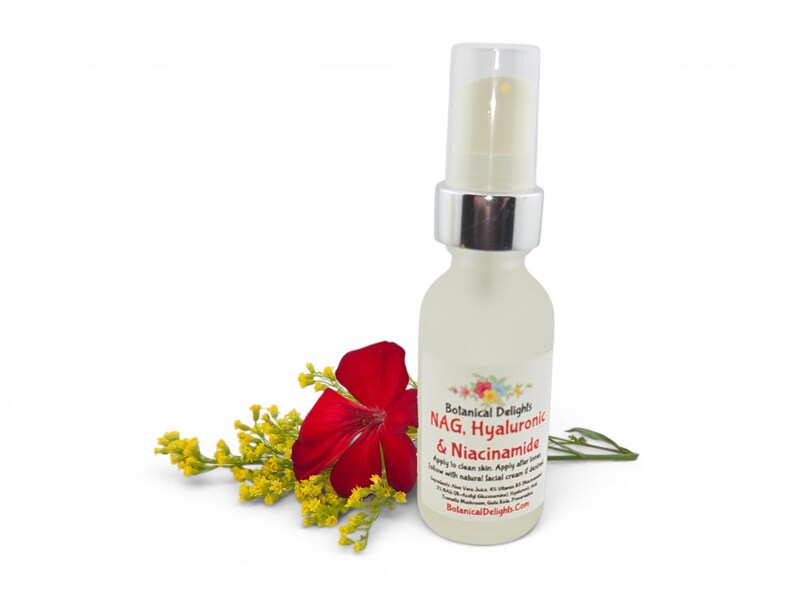 May include: A frosted glass bottle with a silver pump top, labeled "Botanical Delights NAG, Hyaluronic & Niacinamide." A red flower and yellow sprigs are next to the bottle, suggesting a natural skincare product.