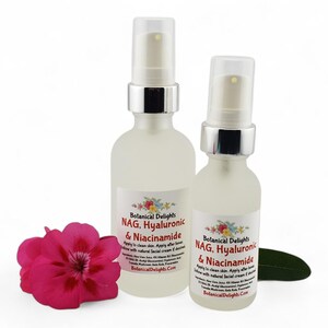 May include: Two frosted glass spray bottles with silver tops, labeled "Botanical Delights NAG, Hyaluronic & Niacinamide." A bright pink flower and a green leaf are in the foreground. The bottles are for skincare.