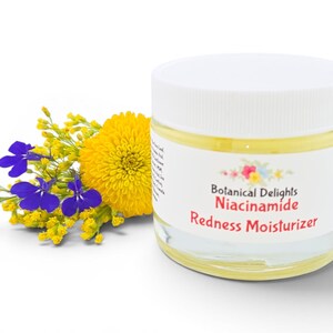 May include: A clear glass jar with a white lid, labeled "Botanical Delights Niacinamide Redness Moisturizer." The jar is next to a bouquet of yellow and blue flowers. The jar contains a yellow liquid.
