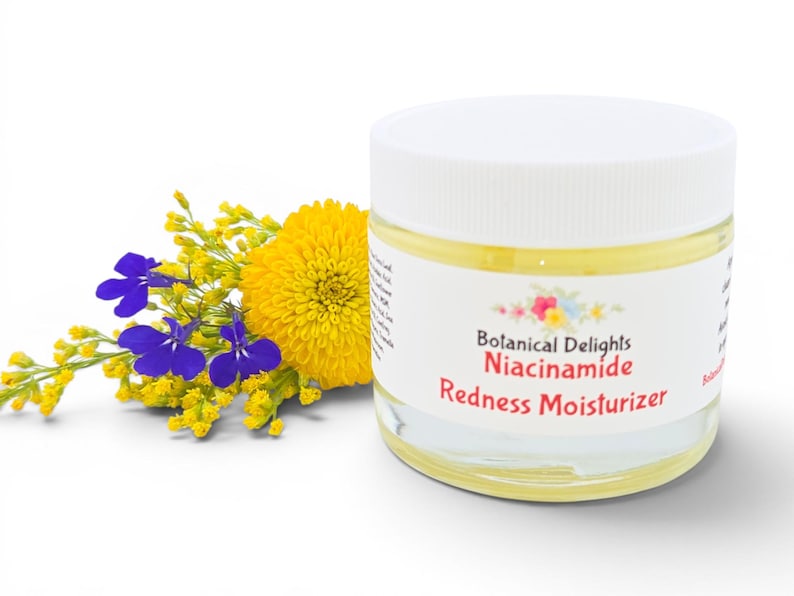 May include: A clear glass jar with a white lid, labeled "Botanical Delights Niacinamide Redness Moisturizer." The jar is next to a bouquet of yellow and blue flowers. The jar contains a yellow liquid.