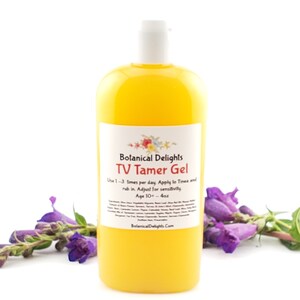 May include: A yellow bottle of TV Tamer Gel by Botanical Delights. The bottle is labeled with the product name and instructions for use. The bottle is sitting on a white surface with purple flowers in the foreground.
