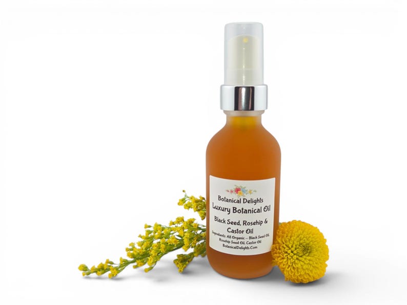 May include: A frosted glass bottle of Botanical Delights Luxury Botanical Oil with a silver pump. The label reads "Black Seed, Rosehip & Castor Oil." Yellow flowers and a yellow pom-pom shaped flower are next to the bottle. The background is white.