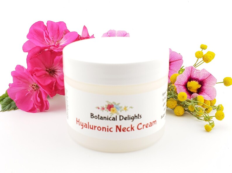 Op de afbeelding: Een witte pot met een wit deksel en een etiket met de tekst "Botanical Delights Hyaluronic Neck Cream". De pot is omringd door roze en gele bloemen.
