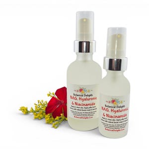 May include: Two frosted glass spray bottles of Botanical Delights facial serum, labeled "NAG, Hyaluronic & Niacinamide." A red flower and yellow sprigs are placed near the bottles. The bottles have silver spray tops and are on a white background.