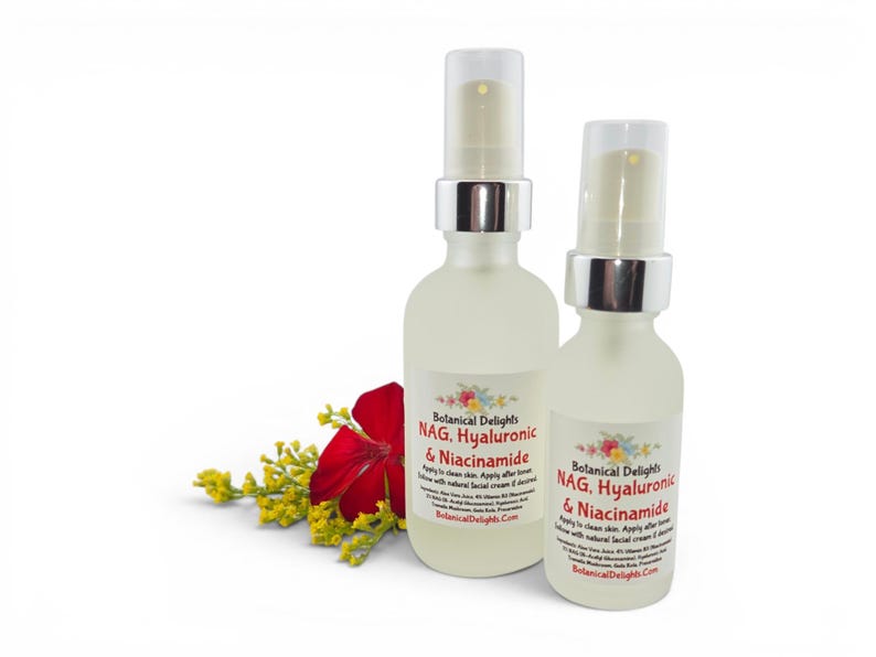 May include: Two frosted glass spray bottles of Botanical Delights facial serum, labeled "NAG, Hyaluronic & Niacinamide." A red flower and yellow sprigs are placed near the bottles. The bottles have silver spray tops and are on a white background.