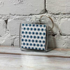 May include: A clear plastic keychain with a blue and white eye pattern. The keychain is attached to a silver ring.