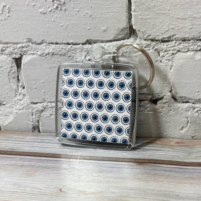 May include: A clear plastic keychain with a blue and white eye pattern. The keychain is attached to a silver ring.