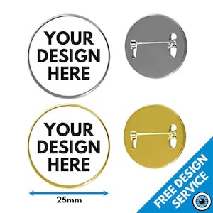 Könnte beinhalten: Zwei runde Anstecknadeln mit einem Durchmesser von 25 mm, eine silberne und eine goldene, mit dem Text "YOUR DESIGN HERE" in Schwarz. Die Anstecknadeln haben eine Nadel auf der Rückseite.