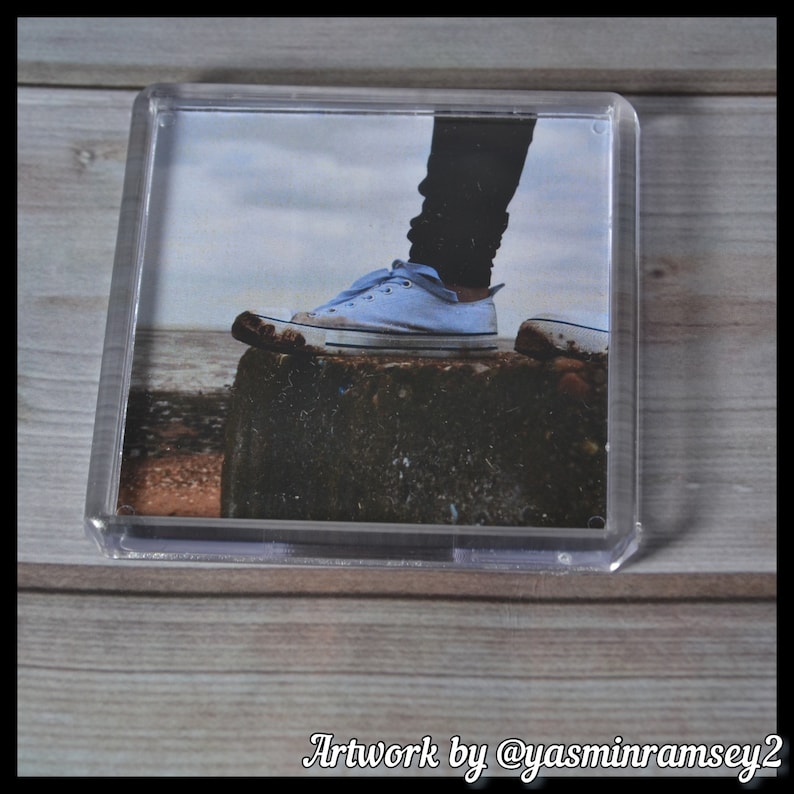 May include: A light blue canvas shoe with white laces resting on a rock. The shoe is partially obscured by a black pant leg.