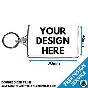 Op de afbeelding: Een transparante sleutelhanger van plastic met een rechthoekige inzet die kan worden gepersonaliseerd met een ontwerp. De sleutelhanger is 70 mm breed en 45 mm hoog. De tekst "YOUR DESIGN HERE" is op de inzet gedrukt.