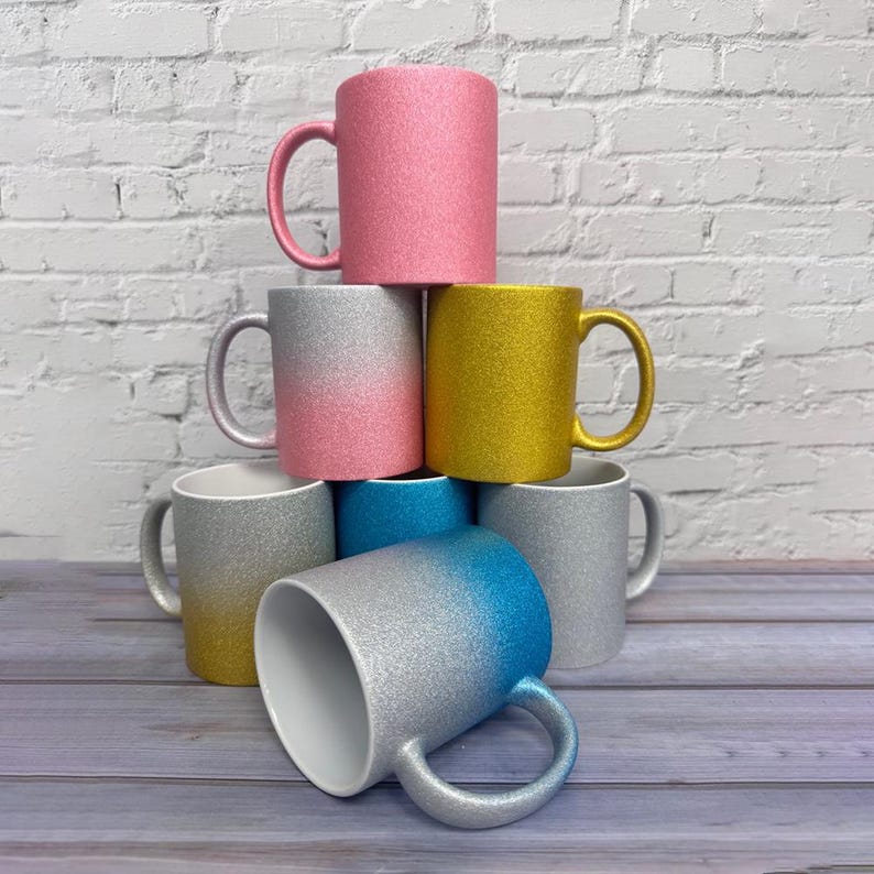 Puede incluir: Una colecci&oacute;n de siete tazas de cer&aacute;mica apiladas en forma de pir&aacute;mide. Las tazas presentan varios acabados con purpurina, incluyendo dise&ntilde;os en rosa s&oacute;lido, dorado s&oacute;lido, degradado de plata a rosa, plata a amarillo y plata a azul.