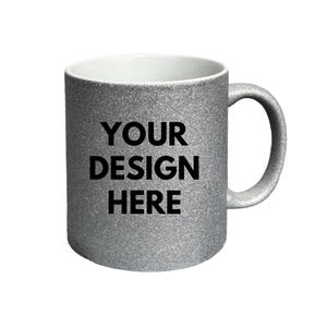 Puede incluir: Una taza de cer&aacute;mica con acabado de purpurina plateada, interior blanco y asa en el lado derecho. La parte frontal de la taza presenta el texto negro "YOUR DESIGN HERE" impreso en una fuente sans-serif negrita, centrado en la superficie.