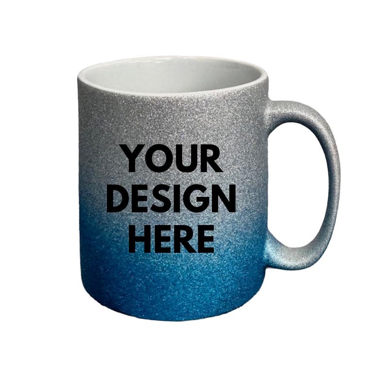 Puede incluir: Una taza de cer&aacute;mica con un acabado brillante que transiciona de plateado en la parte superior a un azul profundo en la base. El texto "YOUR DESIGN HERE" est&aacute; impreso en letras may&uacute;sculas negras en el frente de la taza, que tiene interior blanco.