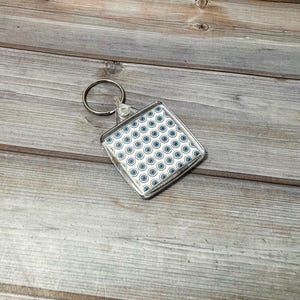 May include: A clear plastic keychain with a square-shaped photo insert featuring a white background with a repeating pattern of blue and white circles.
