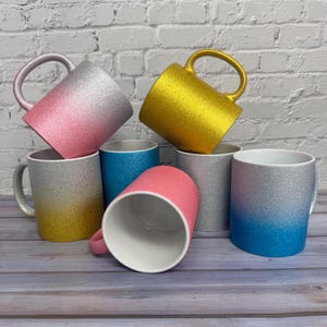 Puede incluir: Una colecci&oacute;n de siete tazas de cer&aacute;mica con varios acabados de purpurina. Las tazas incluyen un degradado de rosa a plata, un dorado s&oacute;lido, un degradado de plata a oro, un azul s&oacute;lido, un plata s&oacute;lido, un rosa s&oacute;lido y un degradado de plata a azul.