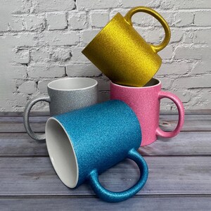 Puede incluir: Un conjunto de cuatro tazas de cer&aacute;mica con acabado brillante en oro, plata, rosa y azul. Cada taza tiene un interior blanco liso y un asa curva. La taza dorada est&aacute; colocada en la parte superior, mientras que las otras est&aacute;n dispuestas debajo.