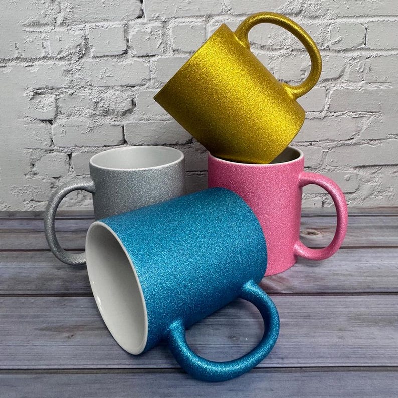Puede incluir: Un conjunto de cuatro tazas de cer&aacute;mica con acabado brillante en oro, plata, rosa y azul. Cada taza tiene un interior blanco liso y un asa curva. La taza dorada est&aacute; colocada en la parte superior, mientras que las otras est&aacute;n dispuestas debajo.