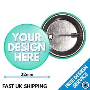 Pode incluir: Um botão redondo de 32 mm com fundo azul turquesa e texto branco que diz "YOUR DESIGN HERE". A parte de trás do botão é prateada com um alfinete.