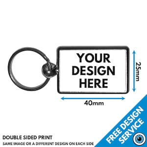 Pode incluir: Um chaveiro de metal prateado com uma etiqueta retangular que diz "YOUR DESIGN HERE". A etiqueta mede 40 mm de largura e 25 mm de altura. O chaveiro é de dupla face, para que você possa adicionar um design diferente a cada lado.