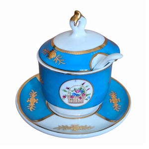 Peut inclure: Un sucrier en porcelaine turquoise vif avec son couvercle et sa soucoupe assortis. L'ensemble présente des bordures dorées, des motifs dorés et un médaillon central circulaire représentant un panier rempli de fleurs colorées. Une petite cuillère blanche est incluse.
