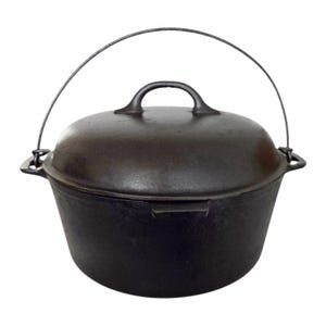 May include: A dark, heavy cast iron Dutch oven with a matching lid and a curved metal bail handle. The pot features a wide, rounded body with integrated side handles and a central loop handle on the lid, showcasing a textured, matte finish.
