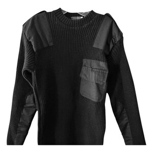 Peut inclure: Pull-over noir à manches longues avec une texture côtelée et deux grands empiècements noirs sur les épaules. Le pull a une grande poche plaquée noire sur le côté gauche.