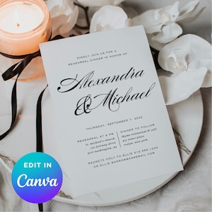May include: A white invitation card with black script text that reads "Alexandra & Michael" for a rehearsal dinner. The card includes event details and is on a white plate with a lit candle and flowers.