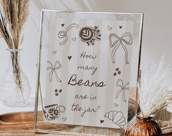 May include: A framed sign with the text "How many Beans are in the jar?" surrounded by coffee-themed illustrations. The sign is in a silver frame, with a neutral background and decorative elements.