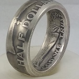 May include: A silver half dollar coin ring with the words "HALF DOLLAR" and "GOD WE TRUST" engraved on the band.