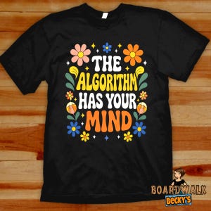May include: A black short-sleeve t-shirt featuring a colorful graphic print with the text THE ALGORITHM HAS YOUR MIND in white and orange lettering, surrounded by stylized flowers in shades of pink, orange, yellow, and blue with green leaves.
