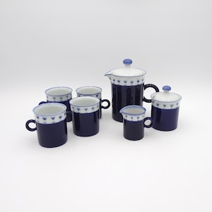 May include: A ceramic tea set featuring a deep navy blue base with a white upper rim decorated with a repeating pattern of small blue flowers. The set includes a lidded teapot, a lidded sugar bowl, a small creamer pitcher, and four matching mugs.