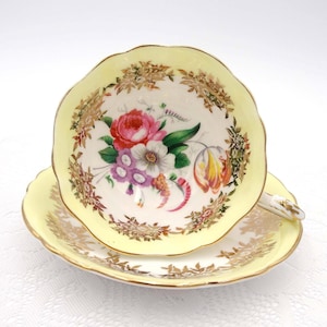 May include: A yellow teacup and saucer with a floral design and gold trim. The cup and saucer have a scalloped edge.