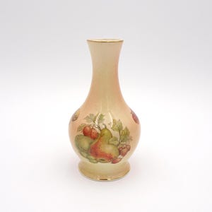 May include: A small, cream-colored ceramic vase with a pear and other fruit design. The vase has a gold rim and a slightly flared base.