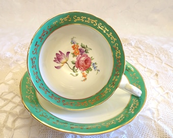 May include: A vintage teacup and saucer set with a floral design. The cup and saucer have a green rim with a gold trim and a white center with a floral pattern.