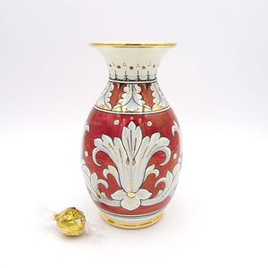 May include: A red and white ceramic vase with gold accents and a floral design. The vase has a round body and a narrow neck.