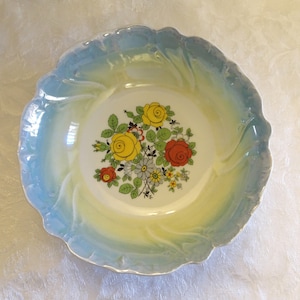 May include: A white ceramic bowl with a blue and yellow glaze. The bowl has a floral design with red, yellow, and white flowers.