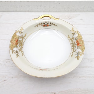May include: A cream-colored, antique porcelain dish with a gold handle and rim. The dish features floral and scrollwork designs in gold, orange, and blue. The center of the dish is white and glossy.