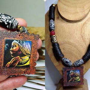 May include: Handmade necklace featuring a pendant with a portrait of a woman in profile. The necklace has black disc beads, patterned beads, and red accent beads. The pendant is framed in a decorative, brown border.