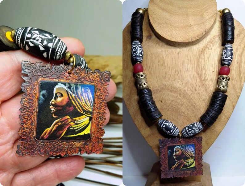 May include: Handmade necklace featuring a pendant with a portrait of a woman in profile. The necklace has black disc beads, patterned beads, and red accent beads. The pendant is framed in a decorative, brown border.