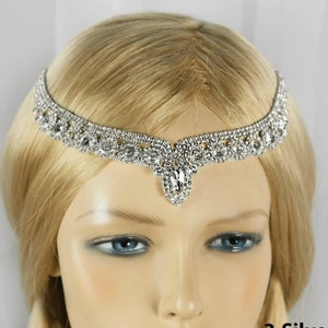 May include: A silver headband with a teardrop-shaped crystal in the center and smaller crystals surrounding it.